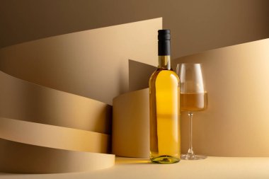 Bottle and glass of white wine on a beige background. Copy space.