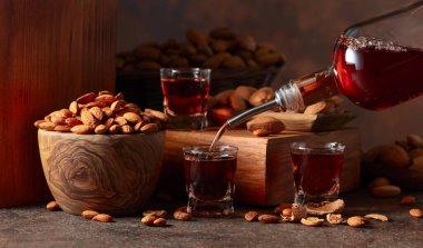 İtalyan likörü Amaretto. Eski bir masada badem fıstıklı. Likör şişeden bardağa dökülür..