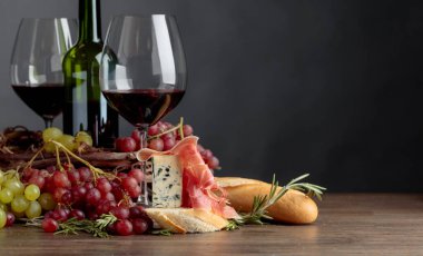 Sandwich with prosciutto, blue cheese and rosemary on a dark background. Delicious snack and red wine.