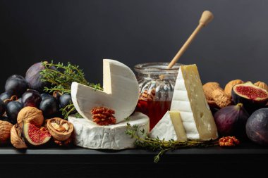 İncirli, üzümlü, cevizli, ballı ve kekikli Camembert peyniri. Siyah arka planda meyveli yumuşak peynir..