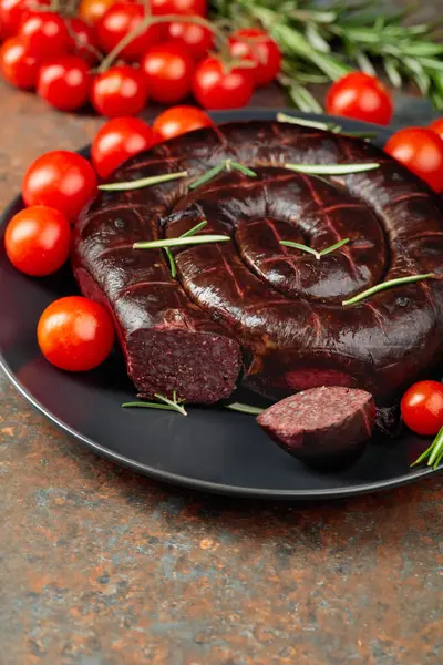 Black pudding or blood sausage with rosemary and tomatoes on a black plate.