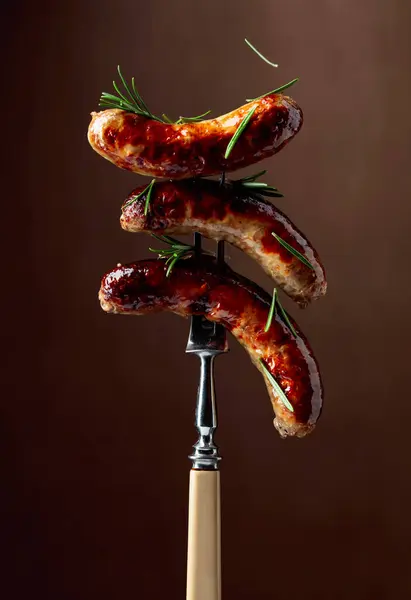 烤巴伐利亚香肠配迷迭香叉子上的香肠撒满了迷迭香 棕色背景 — 图库照片
