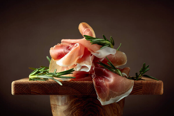 Prosciutto with rosemary on a brown background. Traditional Mediterranean snack.