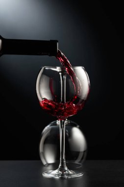 Siyah arka planda şarap bardağına kırmızı şarap dökmek. Arka planda ters çevrilmiş bir cam var..