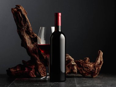 Siyah taş bir masanın üzerinde şişe ve bir bardak kırmızı şarap. Arka planda eski yıpranmış bir pürüz var. Kopyalama alanı ile ön görünüm.