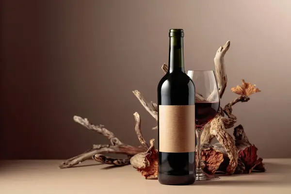 Bottle and glass of red wine with a composition of old wood. Minimalistic composition on a beige background for product branding, identity, and packaging. Copy space.