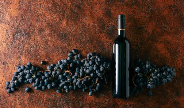 Blaue Trauben Und Eine Flasche Rotwein Auf Braunem Vintage Hintergrund — Stockfoto