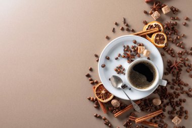 Beyaz fincanda sade kahve. Bej arkaplanda kahve çekirdekleri, tarçın çubukları, anason, karanfil, hindistan cevizi, biber, esmer şeker ve kurutulmuş portakal dilimleri bulunur. Seçici odaklanma. Boşluğu kopyala.