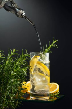 Buzlu, limonlu ve biberiyeli cin tonik. Cin şişeden buz ve limon dilimleriyle bardağa dökülür. Boşluğu kopyala.