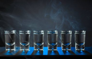 Alkolik votka kadehleri ya da siyah arka planda küçük bardaklarda sert içkiler. Mavi arka ışık. Boşluğu kopyala.