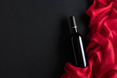 Bottle of red wine with red satin on a black background. Top view.