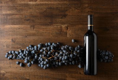 Eski ahşap bir masada mavi üzümler ve bir şişe kırmızı şarap. Boşluğu kopyala.