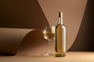 Bottle and glass of white wine on a beige background. Copy space.