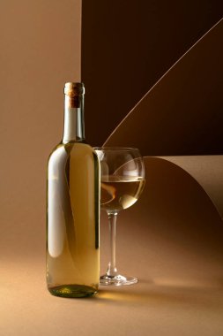 Bottle and glass of white wine on a beige background. Copy space.