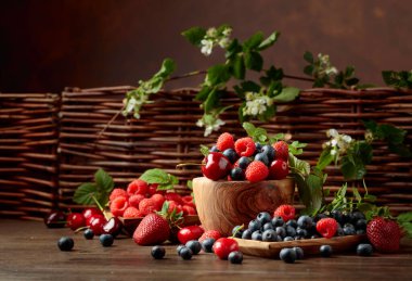 Bahçedeki eski ahşap bir masada çilek, yabanmersini, ahududu ve tatlı kiraz karışımının yakın plan renkli meyveleri. Yapraklı çeşitli meyveler.