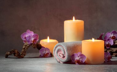 Havlular, orkide çiçekleri ve gri arka planda yanan mumlar. Kopyalama alanı ile kaplıca kavramı.