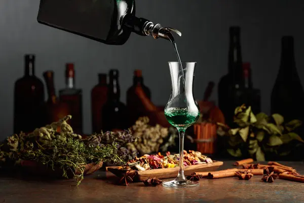 グリーンハーブ酒はヴィンテージボトルからグラスに注がれます テーブルの上に乾燥ハーブ スパイス 古いキッチン用品があります ハーブ医学の概念 — ストック写真
