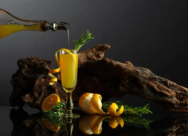 黒い反射の背景に伝統的なイタリアのリキュールリムチェッロ 古いスナッグの背景にローズマリーツイッグを施したレモン酒のグラス 液体をガラスに注入する — ストック写真