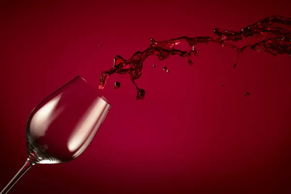 空のワイングラスと赤ワインが赤い背景に飛びつきます コピースペース — ストック写真