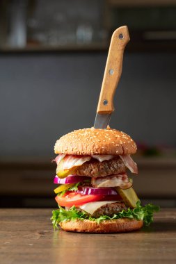 Mutfak masasında bıçaklı taze hamburger. Domatesli hamburger, soğan, korunmuş salatalık, salata, peynir, sığır eti ve pastırma..