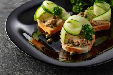 Pate, taze salatalık, kapari ve maydanozlu sandviç. Siyah tabakta ezmeli tost..