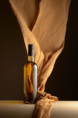 Bir şişe beyaz şarap ve koyu bir arkaplanda bej rengi kumaş..