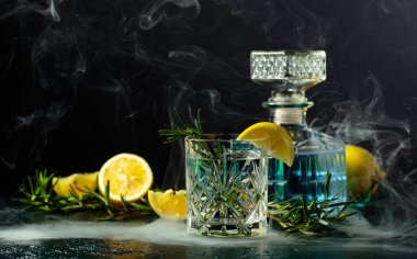 Kristal bardakta limon ve biberiyeli kokteyl cin toniği. Masada tütsülenmiş biberiye eski moda kokteyl..