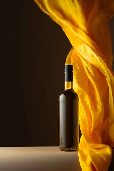 Bottle of white wine and flutters of yellow cloth on a dark background.