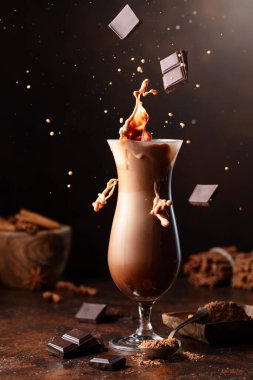 Koyu çikolata parçaları bir bardak kakao içeceğinin içine düşer ve güzel bir su sıçratır..