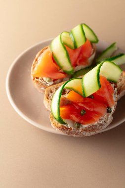 Tütsülenmiş alabalık, krem peynir, taze salatalık ve bej tabakta kapari. Boşluğu kopyala.