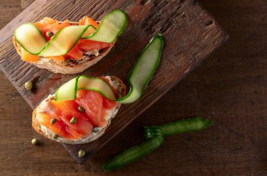 Tütsülenmiş alabalık, krem peynir, taze salatalık ve eski bir kesme tahtasında kapari. Üst görünüm.