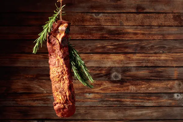 Homemade smoked pork ribs with rosemary branches on a rustic wooden background. Copy space.
