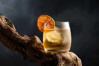 Eski usul buzlu ve kurutulmuş portakal dilimli bir kokteyl eski ahşap bir çıkmazda. Bulutlu gökyüzünün arka planında soğuk bir içecek.