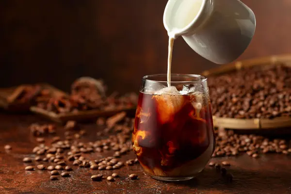 Iced coffee with cream. Refreshing and sweet coffee drink with coffee beans on a brown table.