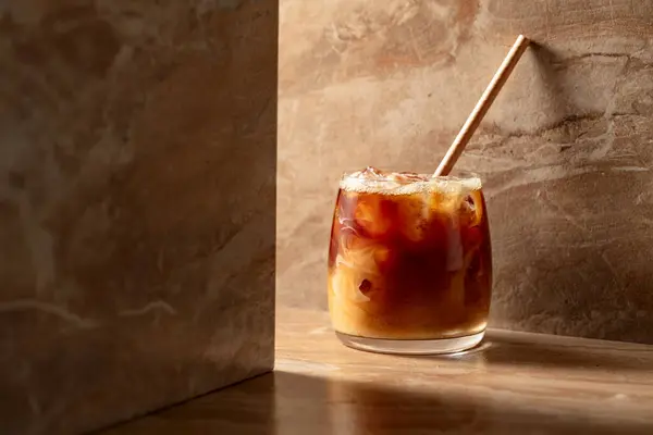 Iced coffee with cream, refreshing and sweet coffee drink on a beige ceramic table.