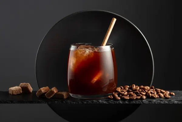 Black coffee with ice on a black background. Iced drink with coffee beans and brown sugar.