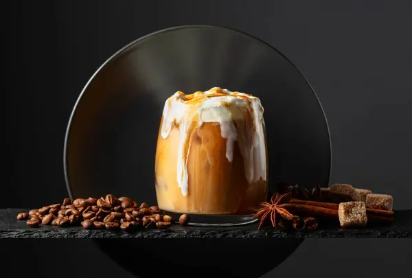 Iced coffee with whipped cream and caramel sauce on a black background. Iced drink with coffee beans, cinnamon, anise, and brown sugar.