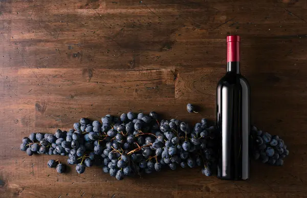 Blue grapes and bottle of red wine on an old wooden table. Copy space.