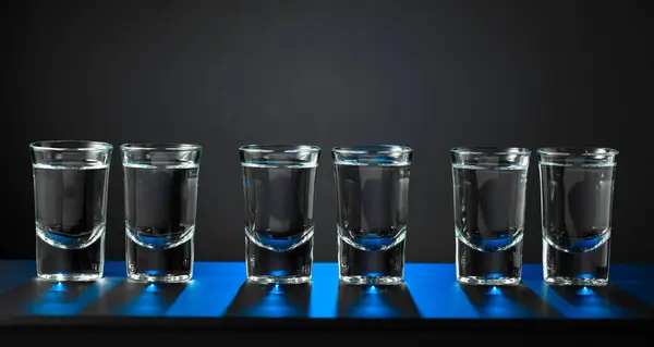 ウォッカのアルコールショットまたは黒い背景に小さな眼鏡で強い飲み物 ブルーバックライト コピースペース ロイヤリティフリーのストック画像