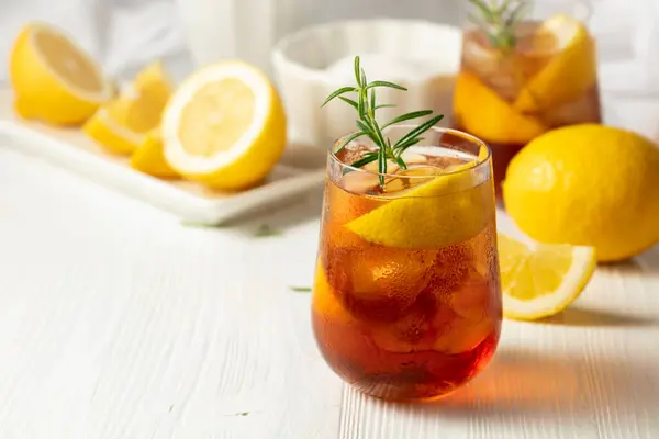 冰茶或含冰的酒精鸡尾酒 迷迭香和柠檬片放在白桌上 新鲜健康的冷柠檬饮料 冰茶和柠檬茶 图库图片