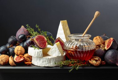 İncirli, üzümlü, cevizli, ballı ve kekikli Camembert peyniri. Siyah arka planda meyveli yumuşak peynir..