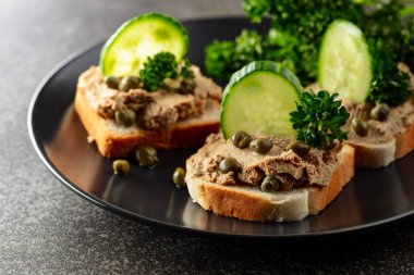 Pate, taze salatalık, kapari ve maydanozlu sandviç. Siyah tabakta ezmeli tost..