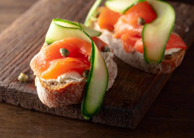 Tütsülenmiş alabalık, krem peynir, taze salatalık ve eski bir kesim tahtasında kapari..