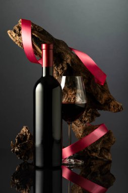 Siyah yansıtıcı arka planda bir şişe kırmızı şarap. Arka planda kırmızı saten kurdeleli yıpranmış eski bir pürüz var. Pahalı şarap kavramı.