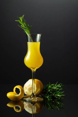 Siyah yansıtıcı arka planda biberiye dalı olan geleneksel İtalyan likörü Limoncello..