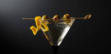 Siyah arka planda yeşil zeytinli ve limon kabuklu klasik sek martini kokteyli. Metnin için boş yer.