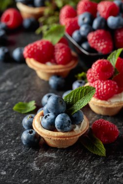 Siyah arka planda naneli taze ahududu ve yaban mersinli küçük tartlar..