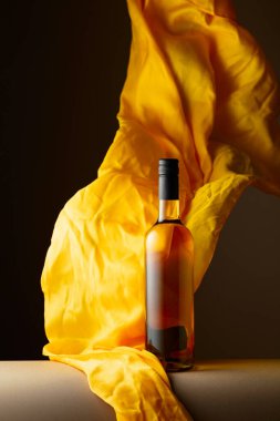 Bir şişe beyaz şarap ve koyu bir arka planda çırpınan sarı kumaş..
