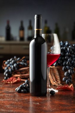 Şarap şişesi ve mavi üzümlü bir bardak şarap. Arka plandaki tezgahta çeşitli şarap şişeleriyle. Önplana odaklan.
