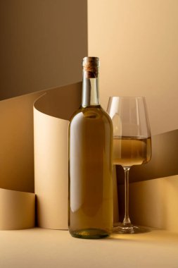 Bottle and glass of white wine on a beige background. Copy space.